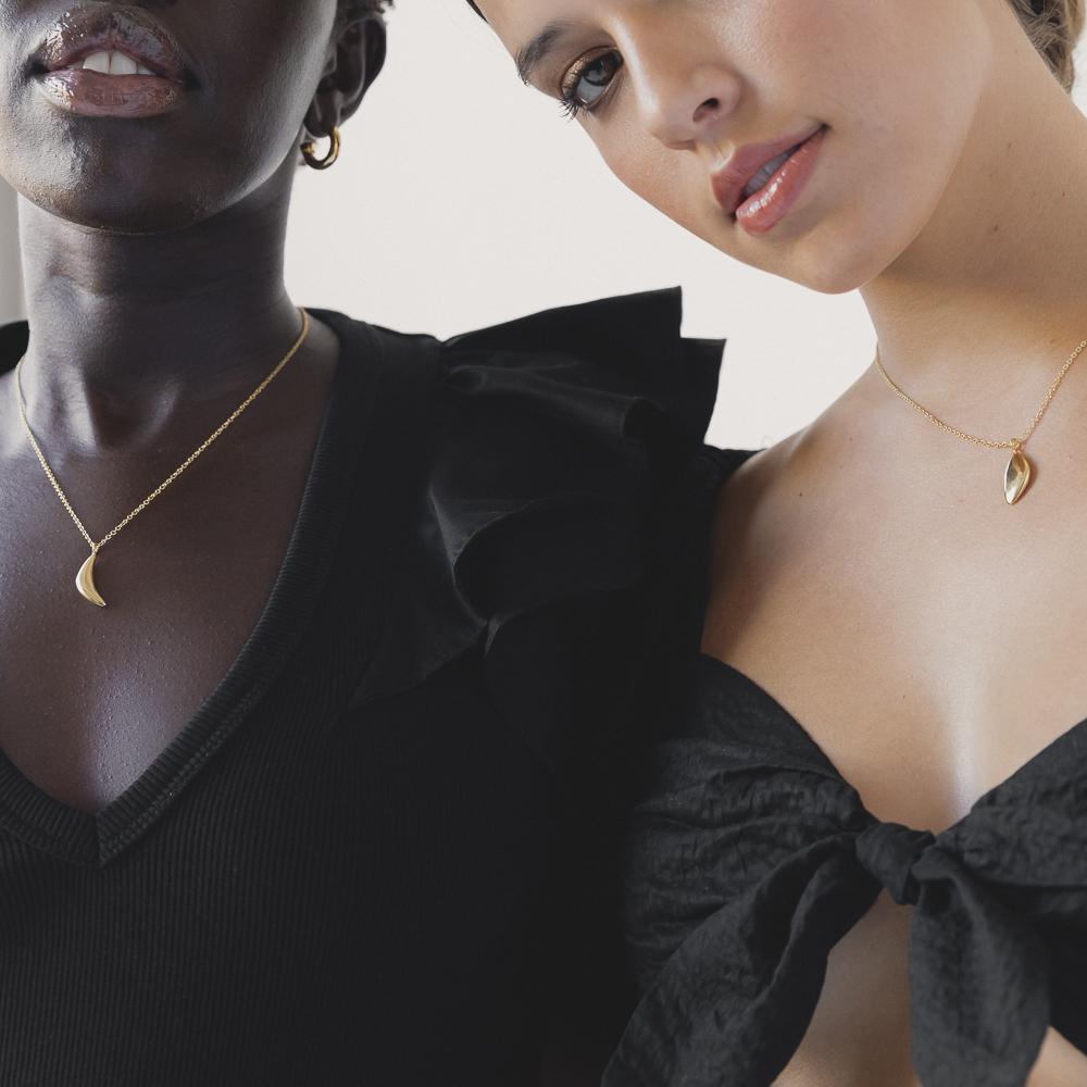 two women in black gowns, both wearing minimal gold chains with pendants around their necks