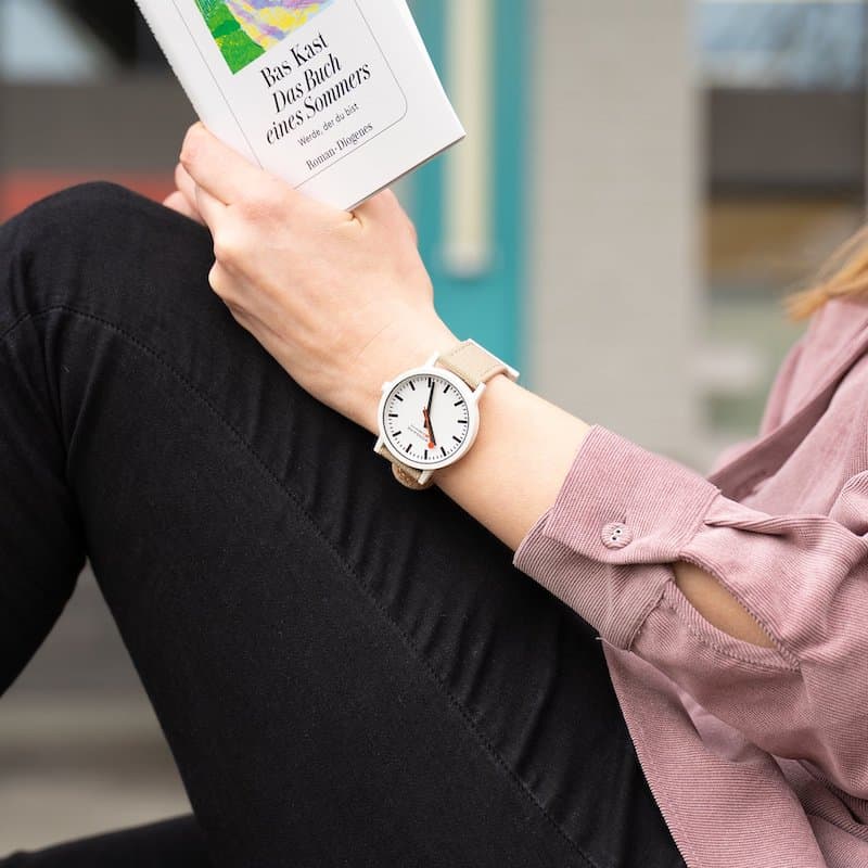 Woman reading a book, and wearing a Mondaine watch 