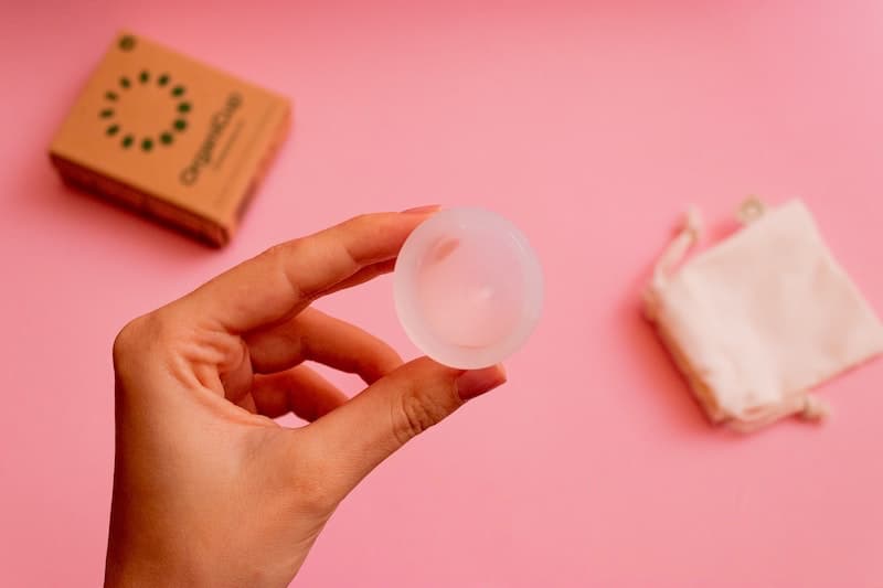 woman's hand holding a menstrual cup - against a pink background