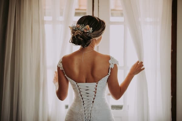 woman wearing a secondhand vintage wedding dress and looking out the window