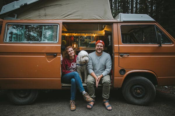 founders of Camp Brand Goods sustainable outdoor clothing brand sitting in their camper van with their dog.
