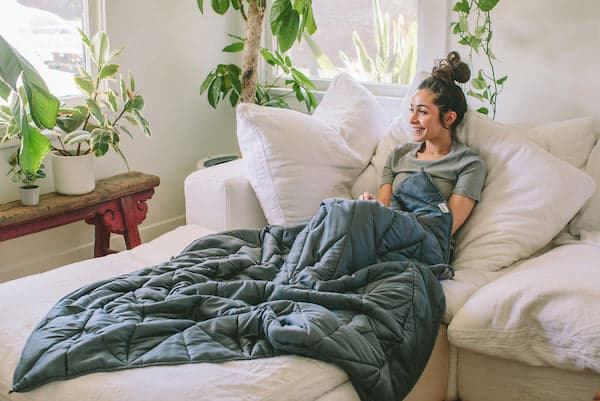 woman sitting on a couch with a grey weighted blanket covering her
