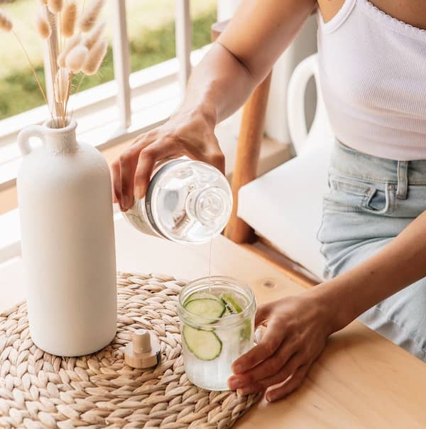 woman pouring cucumber infused water into a glass