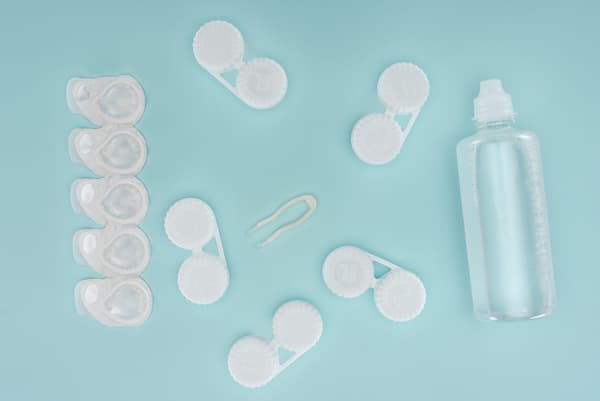contact lens blister packs, lens cases and one lens solution bottle all laid out on a light blue surface