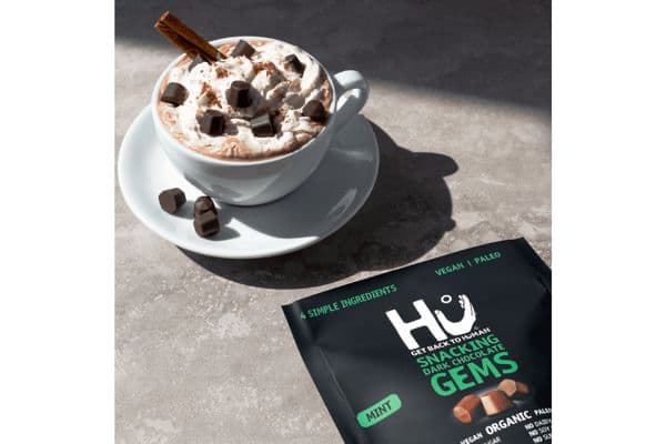 Hu Kitchen sustainable snacks pack along with a mug of hot chocolate