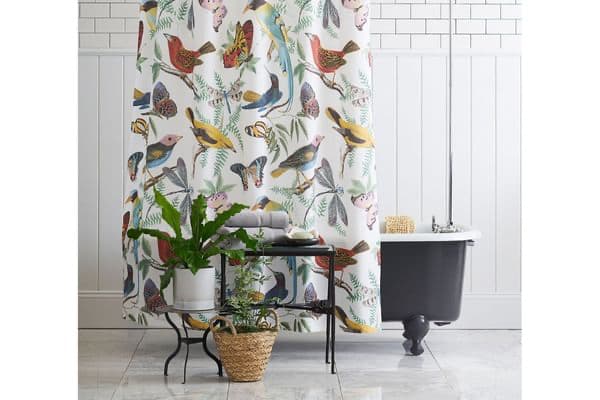 Pottery Barn's bird print linen shower curtain pictured around a black bathtub, grey towels and plants