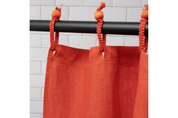 Close-up of Rawganique's non-toxic shower curtain in brick red, hanging from macrame curtain rings