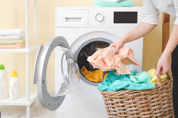 woman loading clothes from the laundry basket into the washing machine