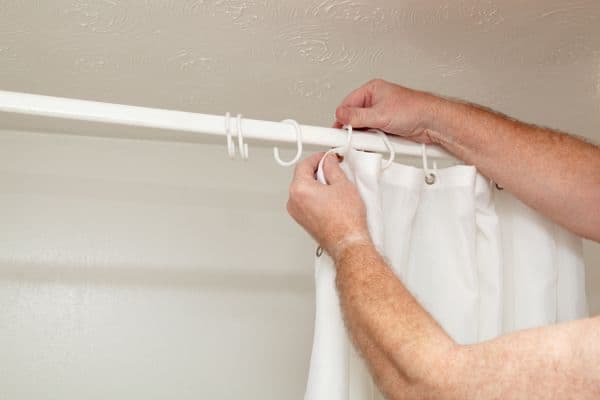 a man unhooking the shower curtain from the curtain rod