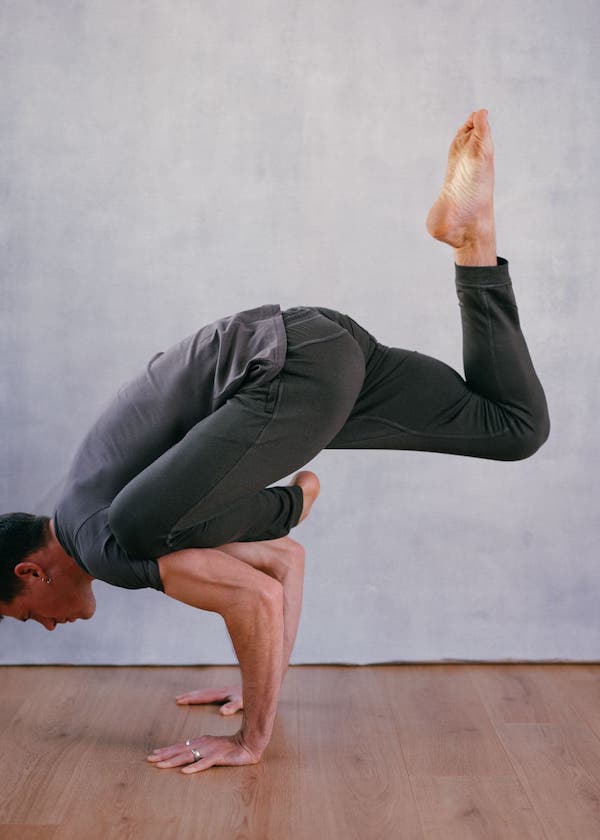 a man doing a modified hand stand, wearing grey t-shirt and grey yoga pants